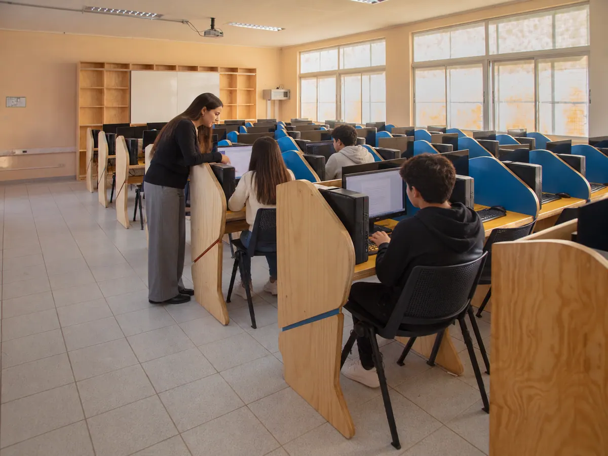Docente acompañando a una estudiante en la sala de informática